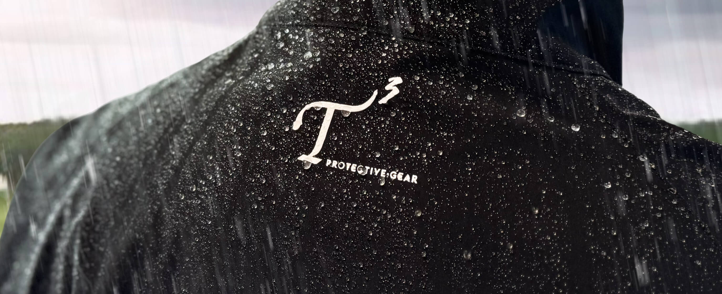 Behind shoulder view of man wearing a black T3 Protective Gear rain jacket at a rainy golf course.