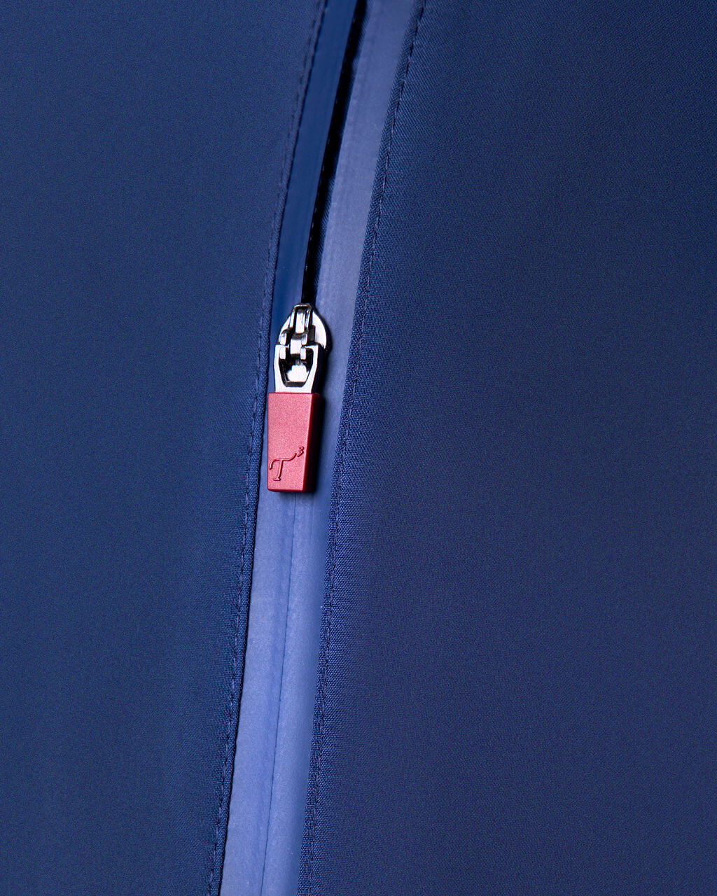Close-up of a blue zipper with a red tag featuring a logo on a matching blue background.